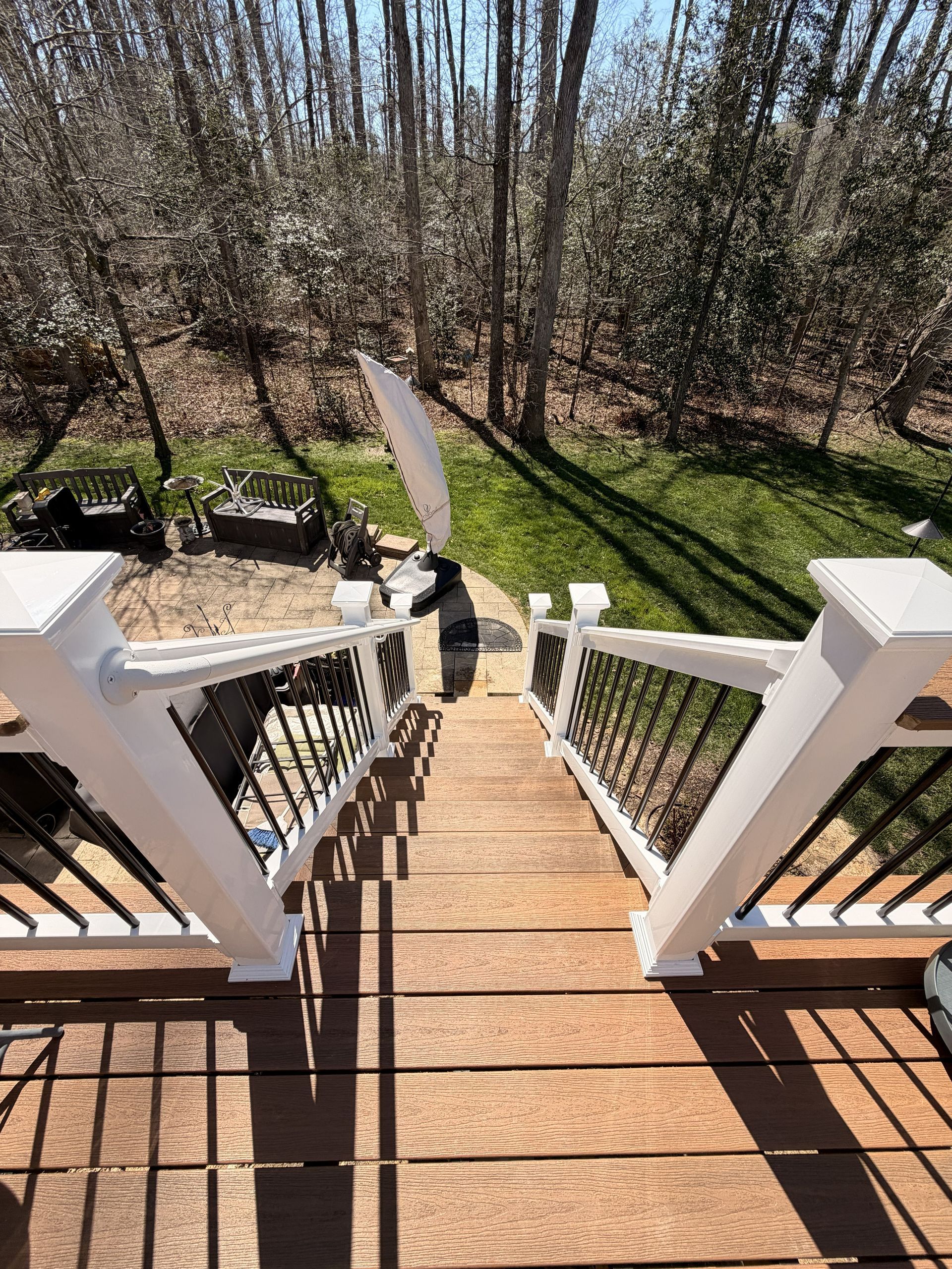 Wooden front steps descend to a sunlit backyard with trees, grass, and a narrow path.