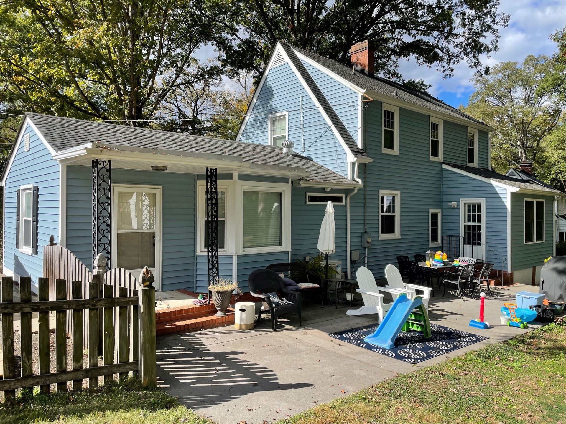 Blue house with white trim, front porch, and a fenced yard with children's toys in the driveway.