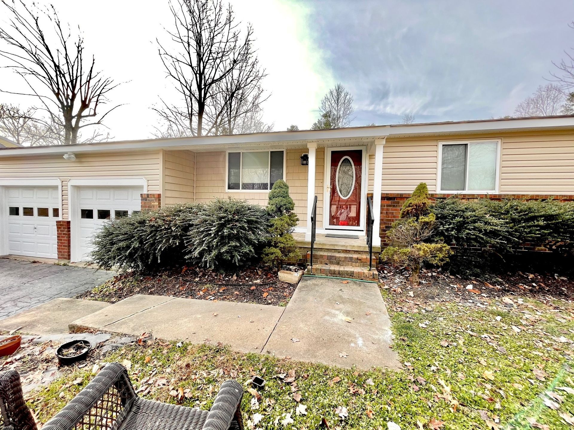 Single-story brick house with garage, red front door, and snowy front yard shrubs