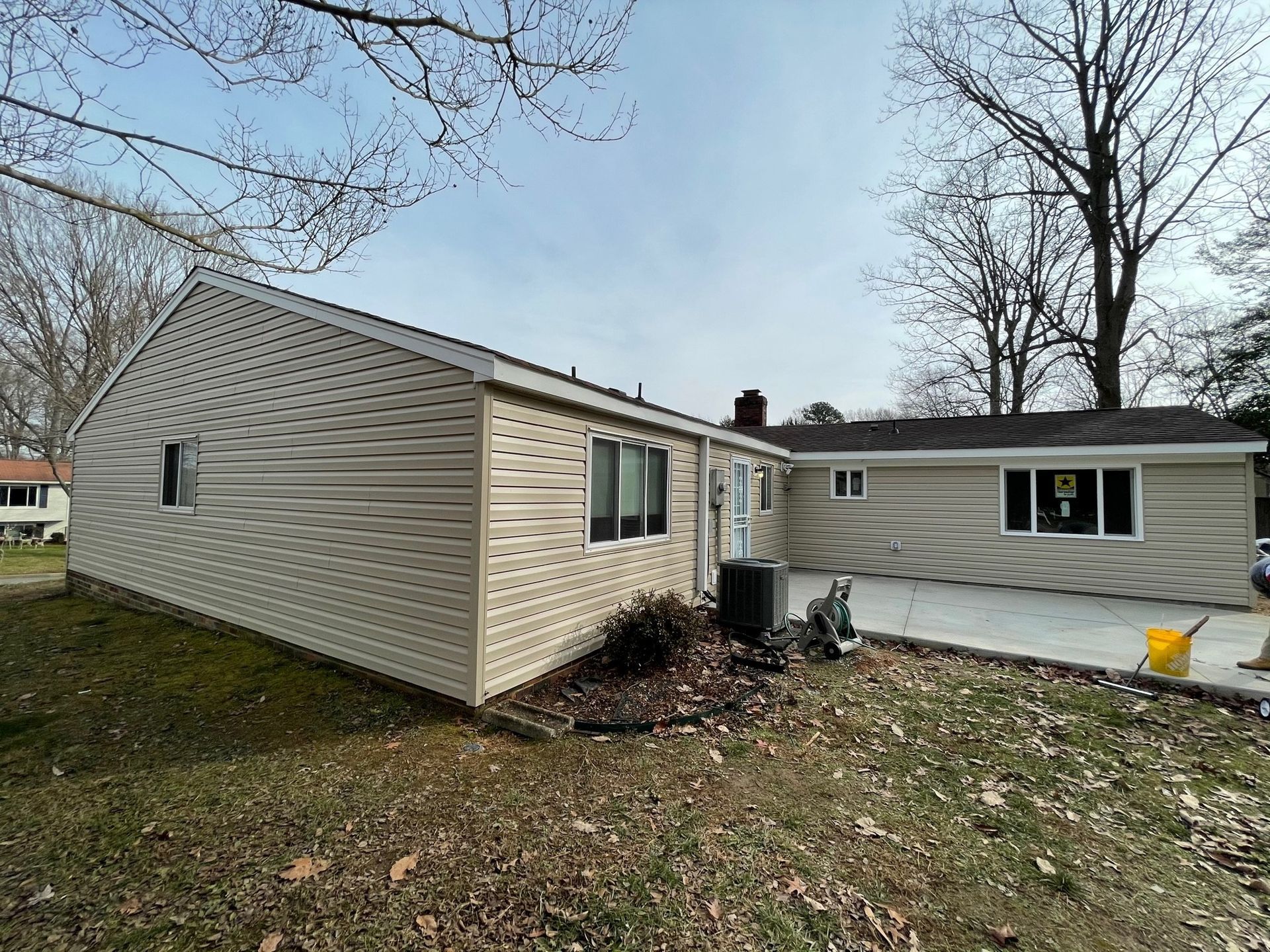 Two beige mobile homes connected by a small entryway on a leaf-covered yard