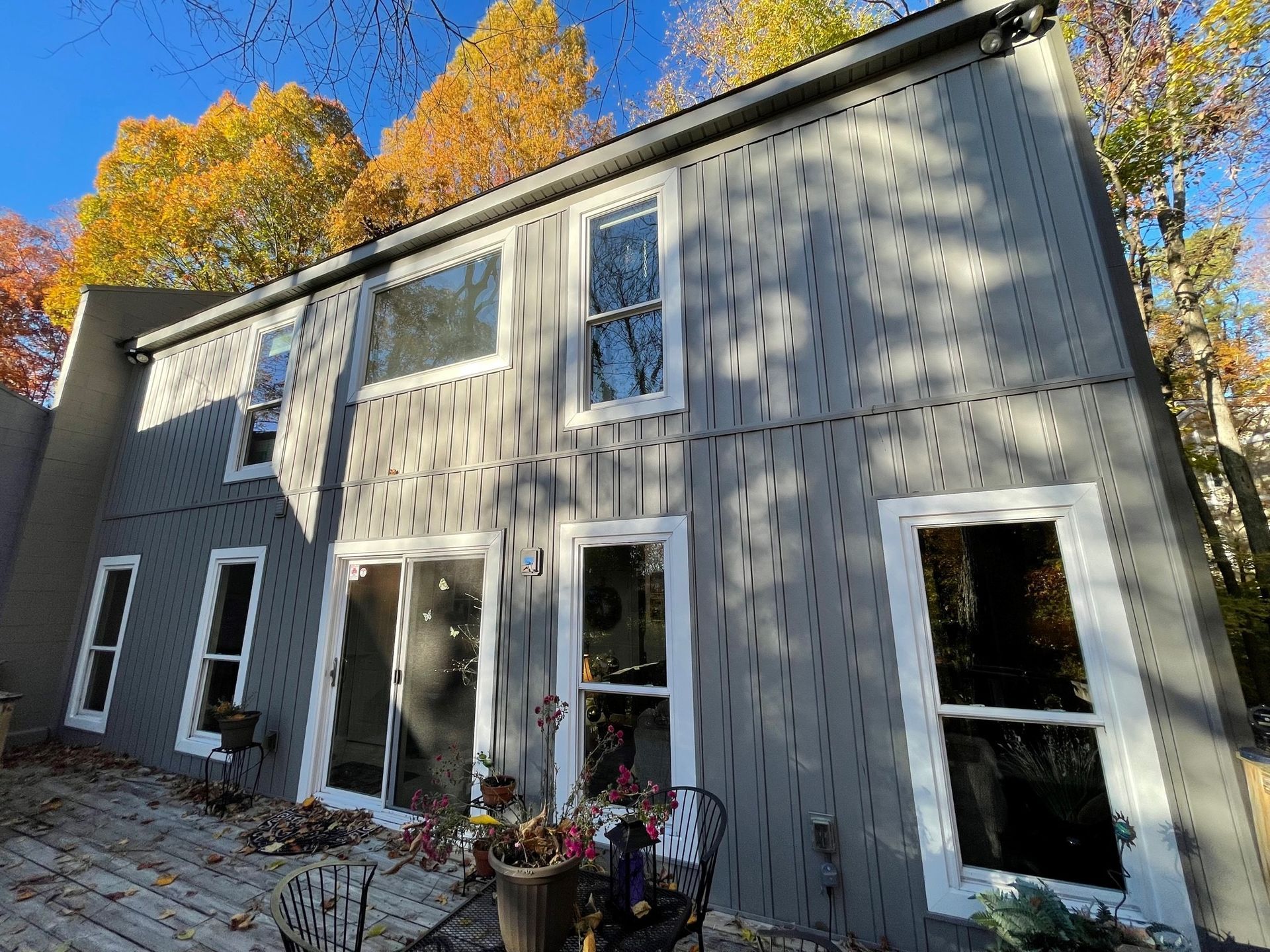 Modern gray house exterior with tall windows and autumn trees overhead
