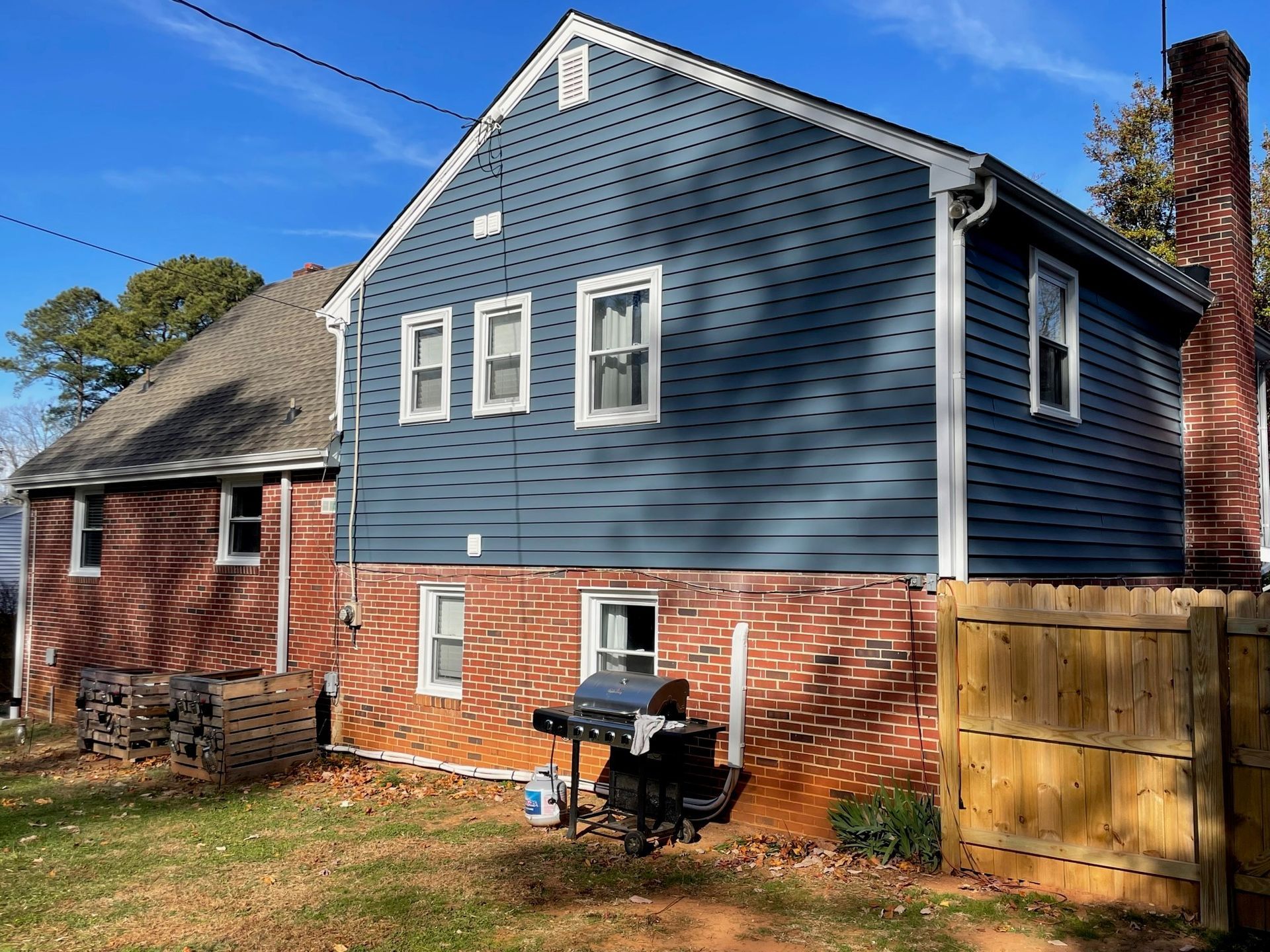 Blue and red house exterior with a wooden fence and a grill in the yard