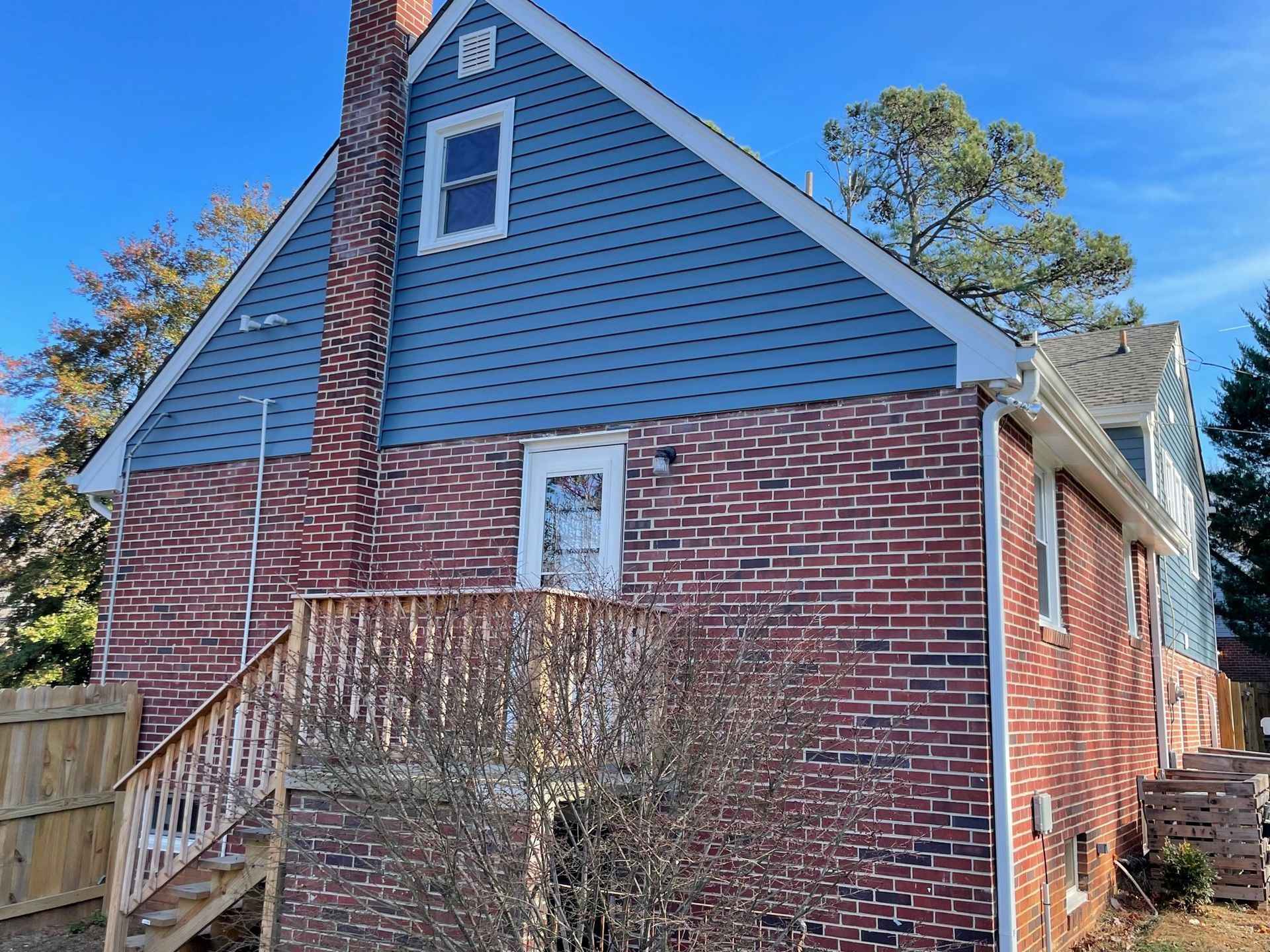 Brick house with blue siding, white trim, and an exterior staircase under a clear sky