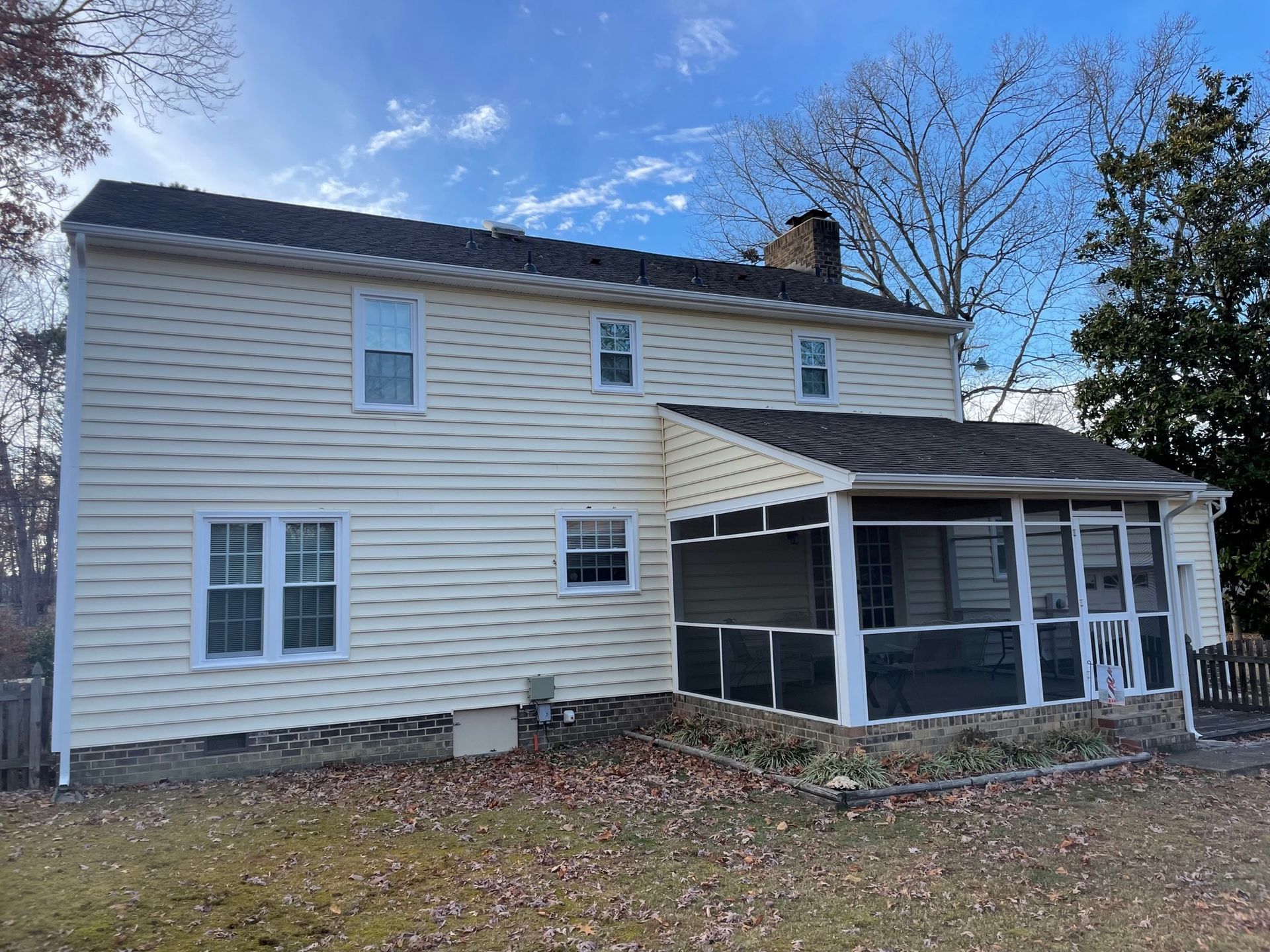 Two-story white house with screened porch and leaf-covered yard under blue sky
