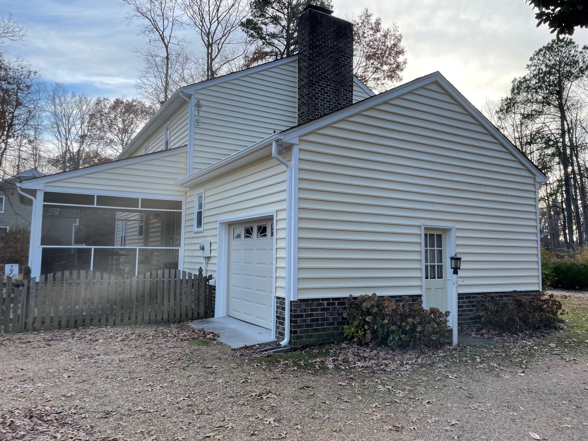 White house with a chimney, attached carport, and garage door in a wooded yard