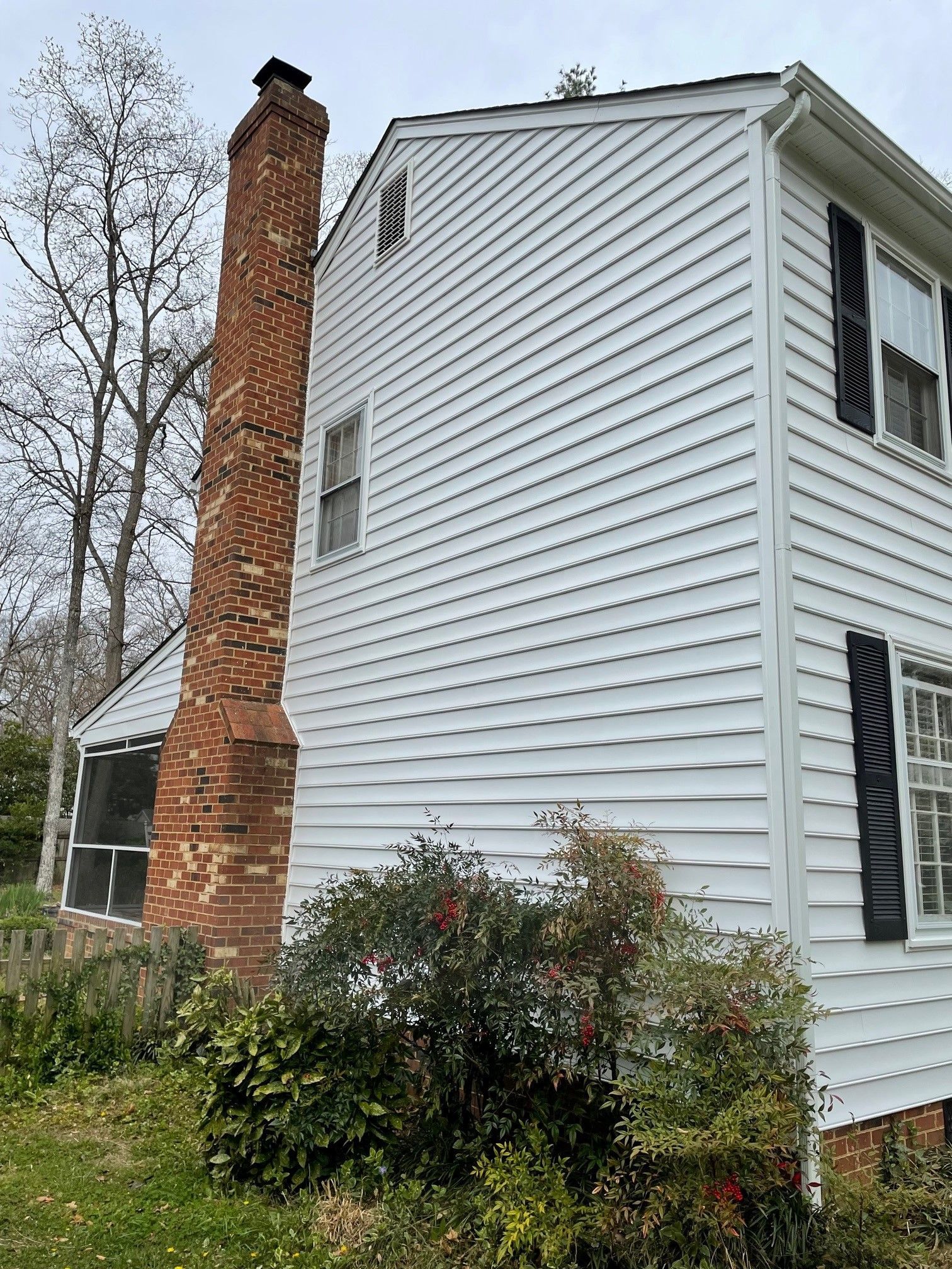 White two-story house with brick chimney, black shutters, and screened porch amid leafless trees