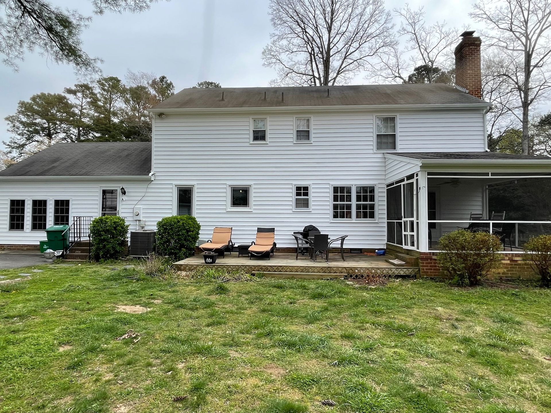 White two-story house with a screened porch, patio chairs, and a grassy yard under bare trees.
