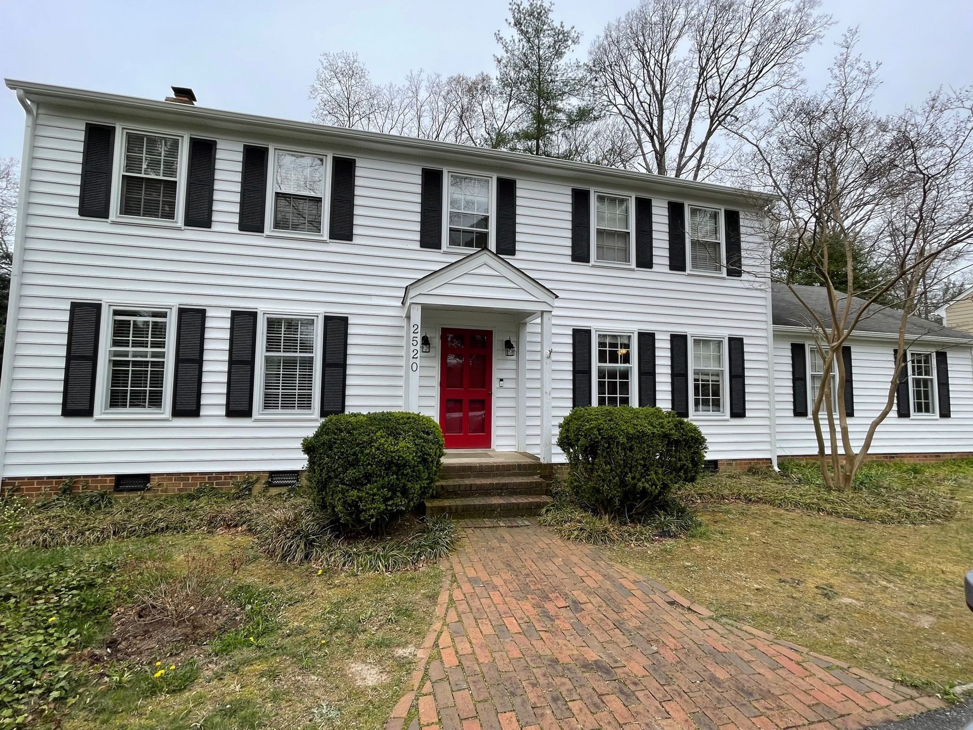 White two-story house with black shutters, red front door, and brick walkway