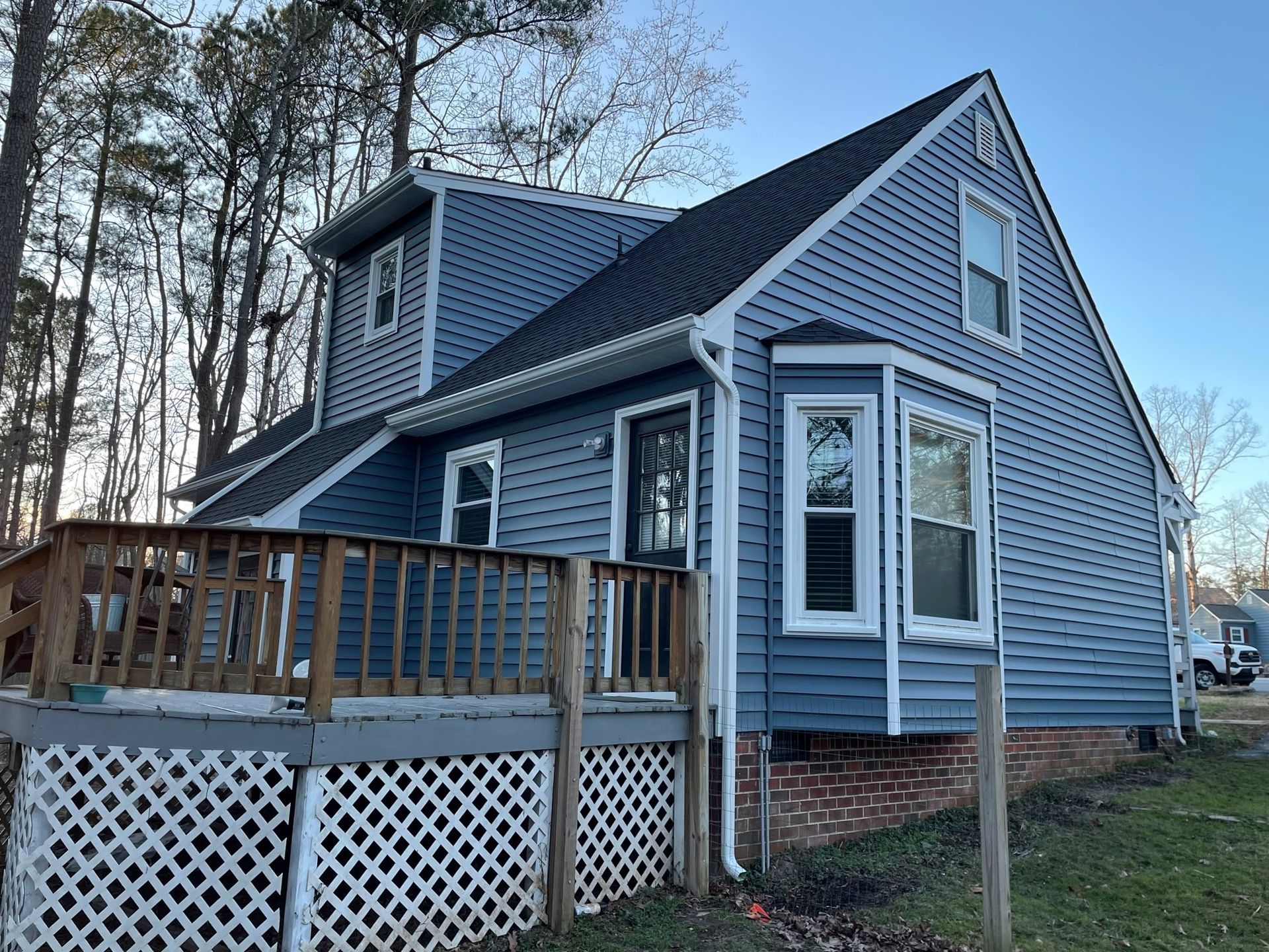 Blue house with a wooden deck and white lattice siding in a wooded yard