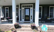 Front porch with white columns, black door, and two chairs on either side.