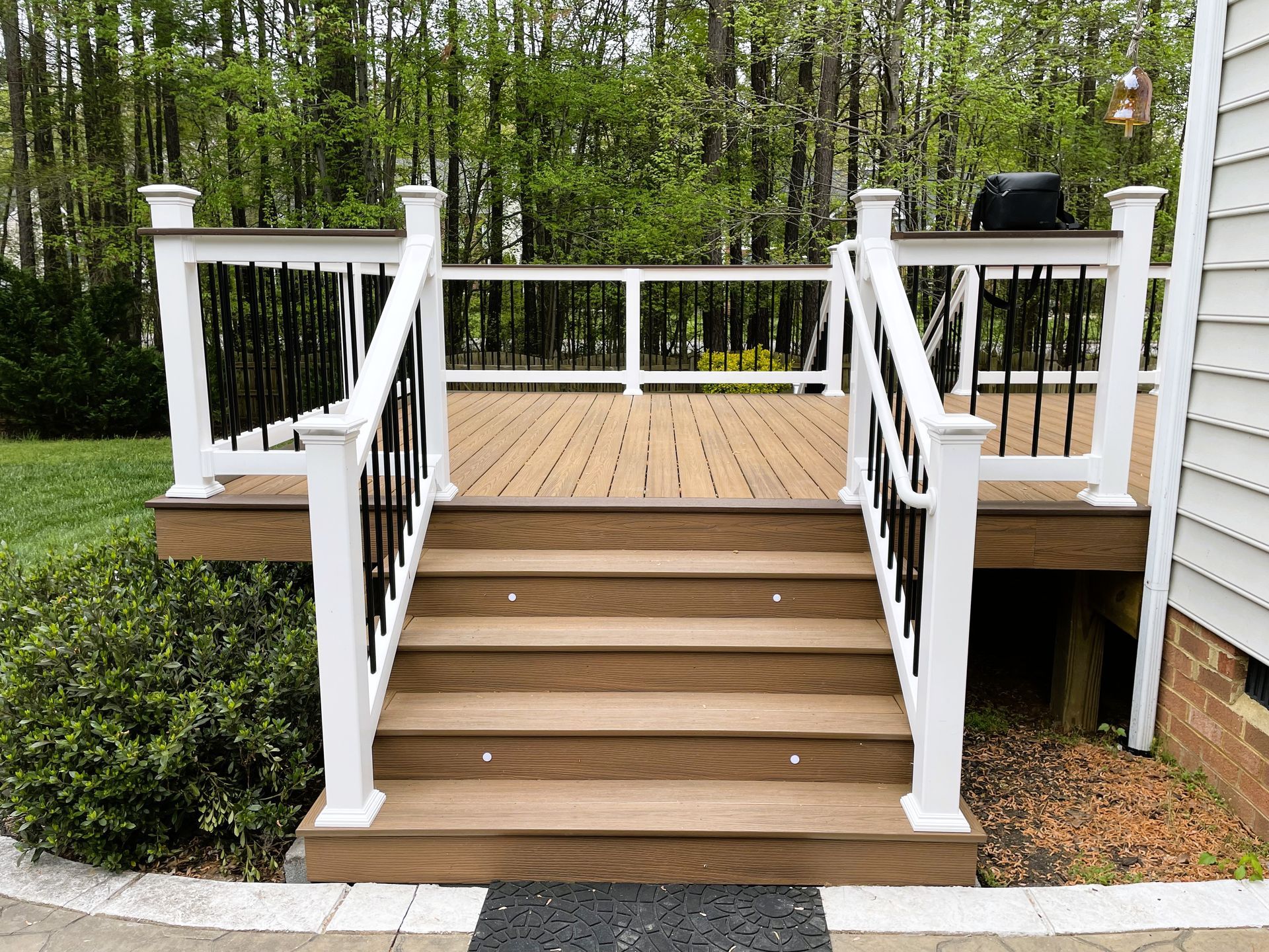 White wooden deck stairs with railings leading to a small raised deck in a wooded backyard.