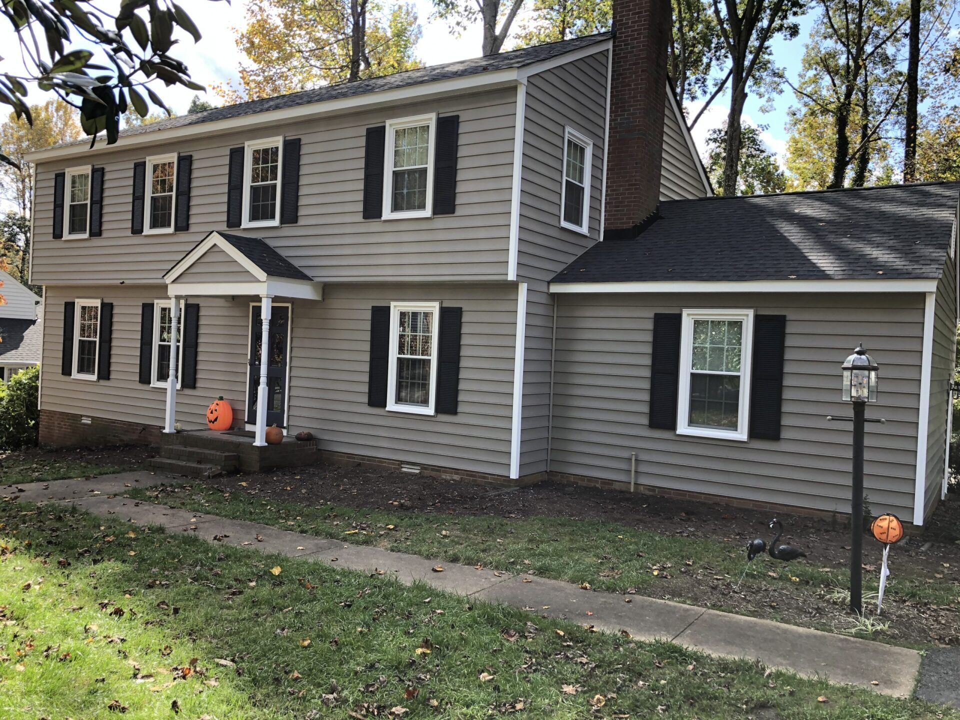 Two-story gray house with white trim and black shutters, front porch, and a large attached garage in a leafy yard