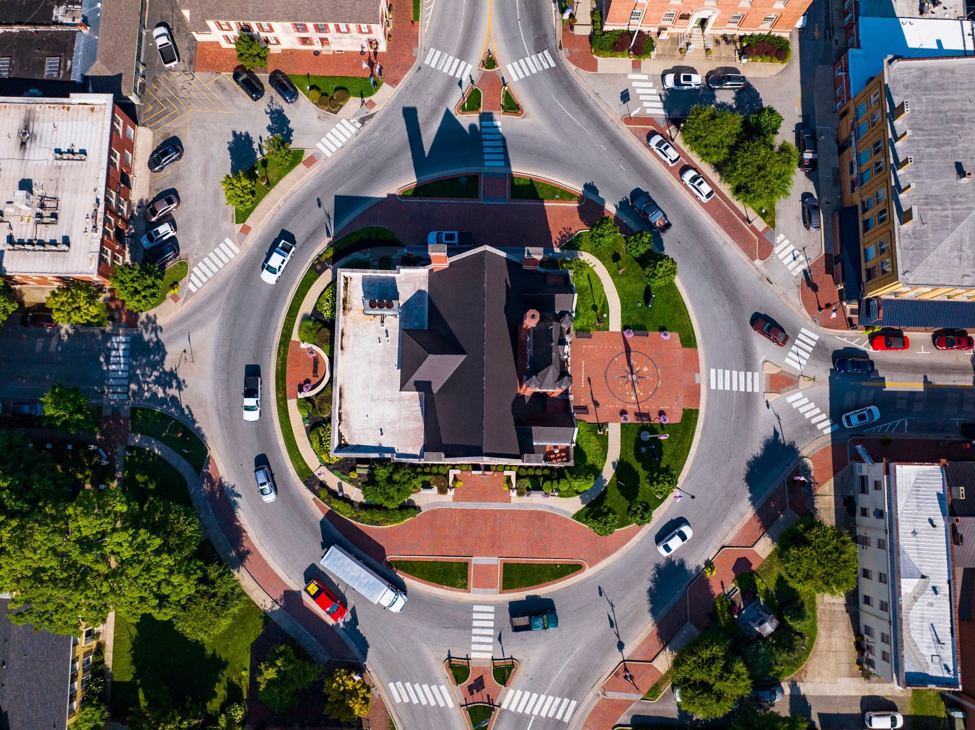 Aerial view of a roundabout with a large house in the center and cars on surrounding streets.