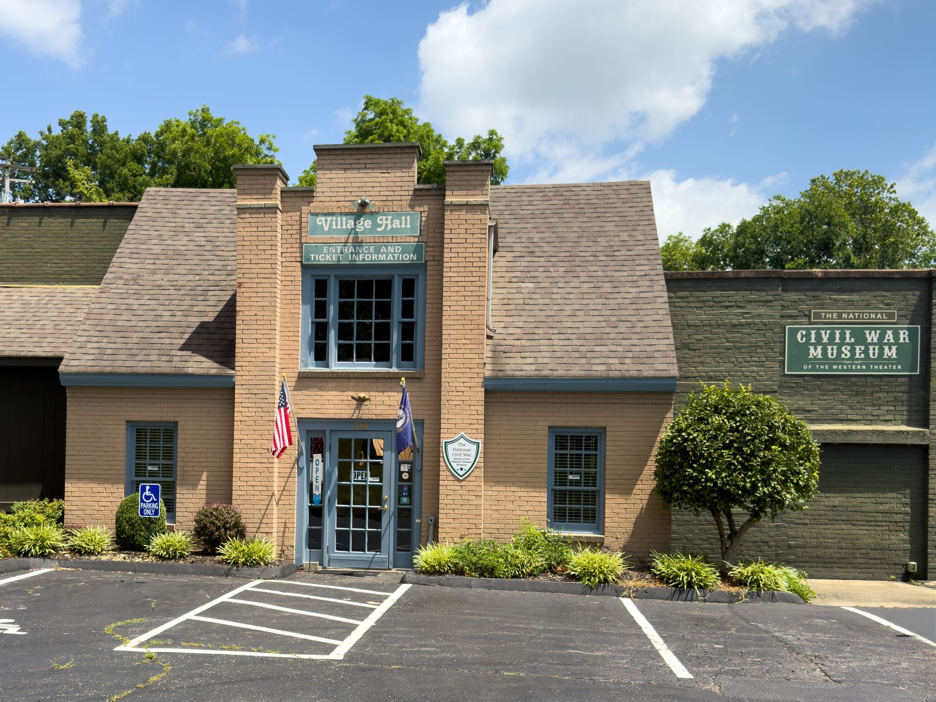 Historic brick building with green roof, American flag, and parking spaces in front