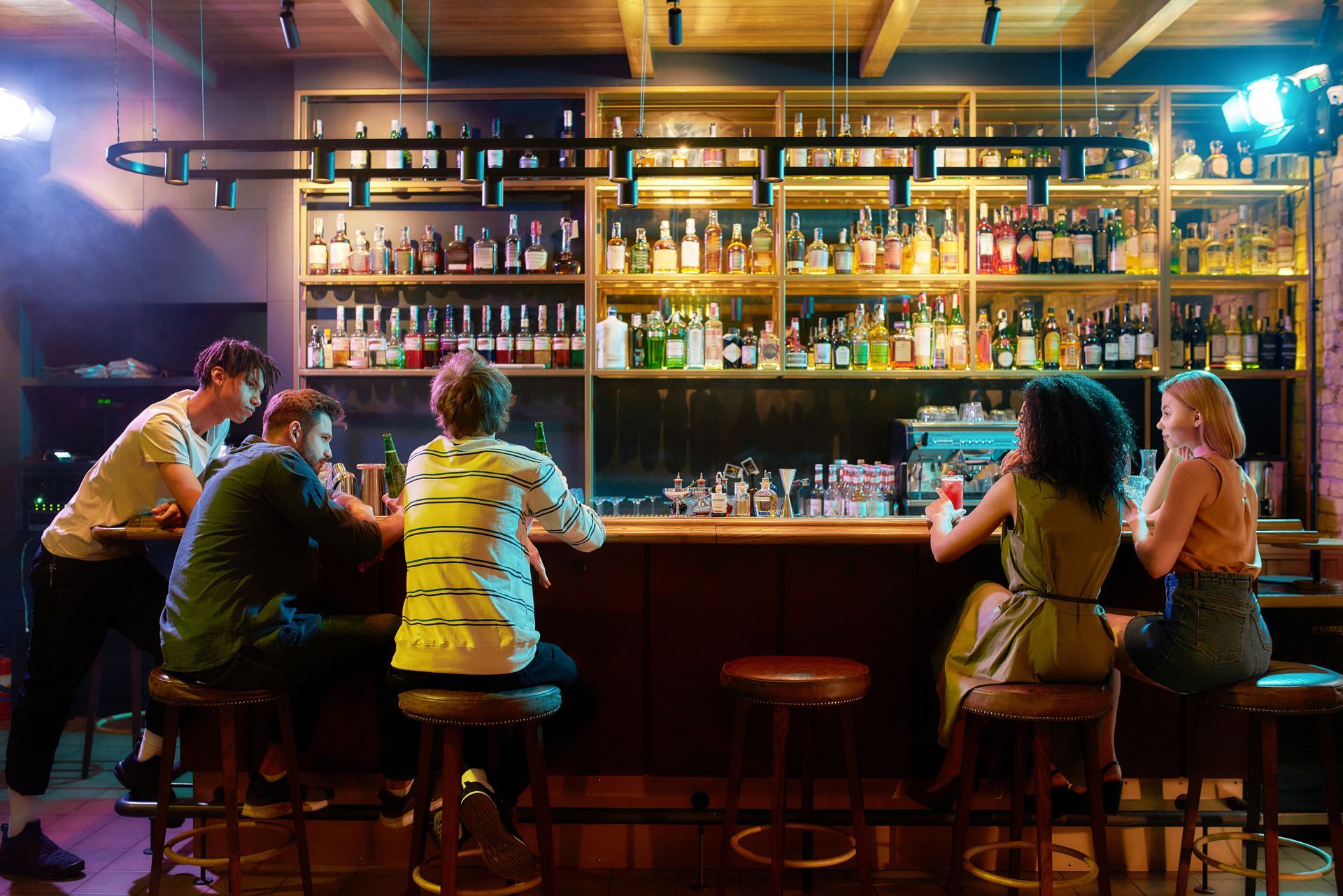 People seated at a warmly lit bar with shelves of bottles behind the counter