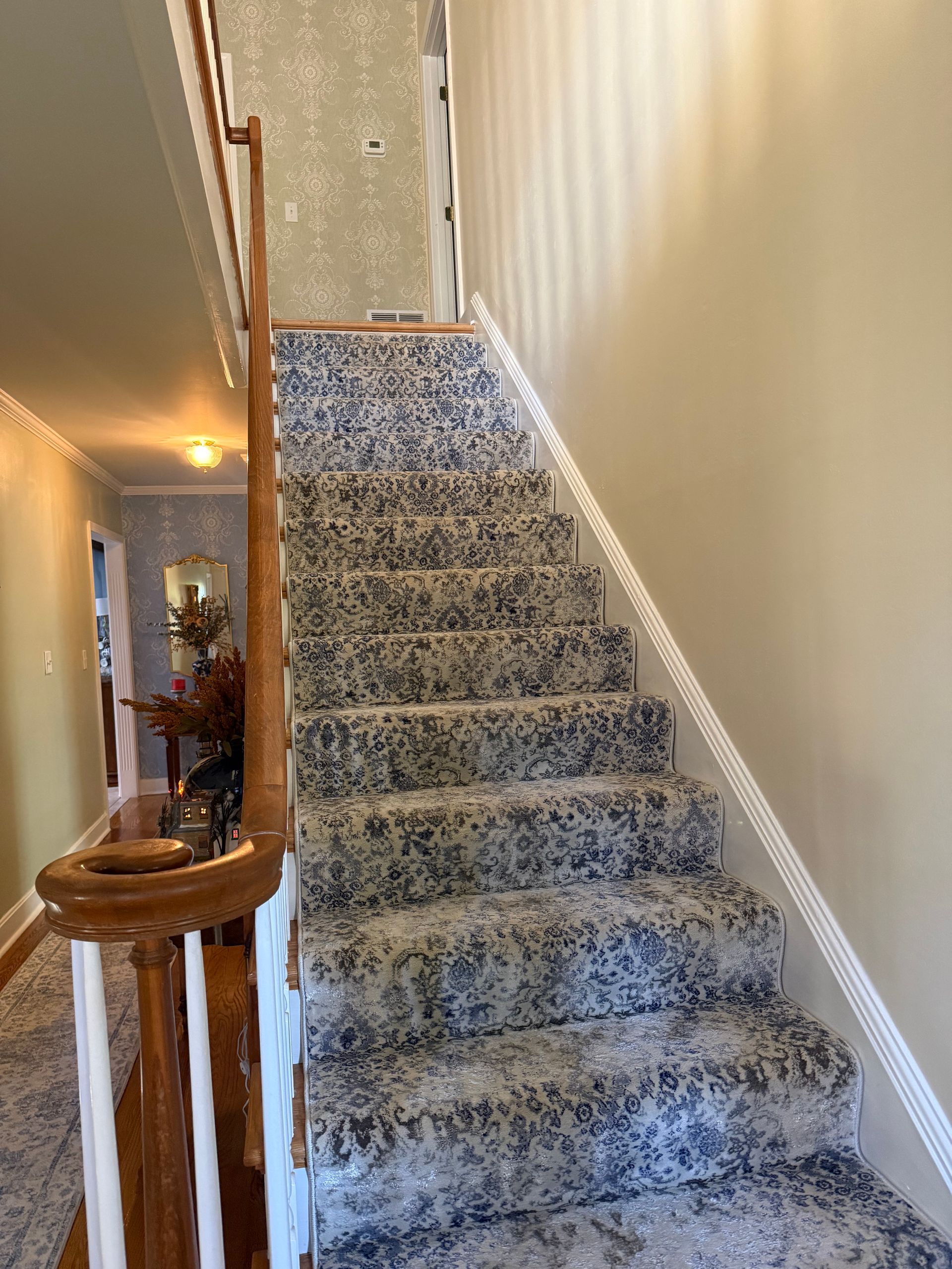 Carpeted staircase with beige walls, wooden banister, and hallway landing at the top