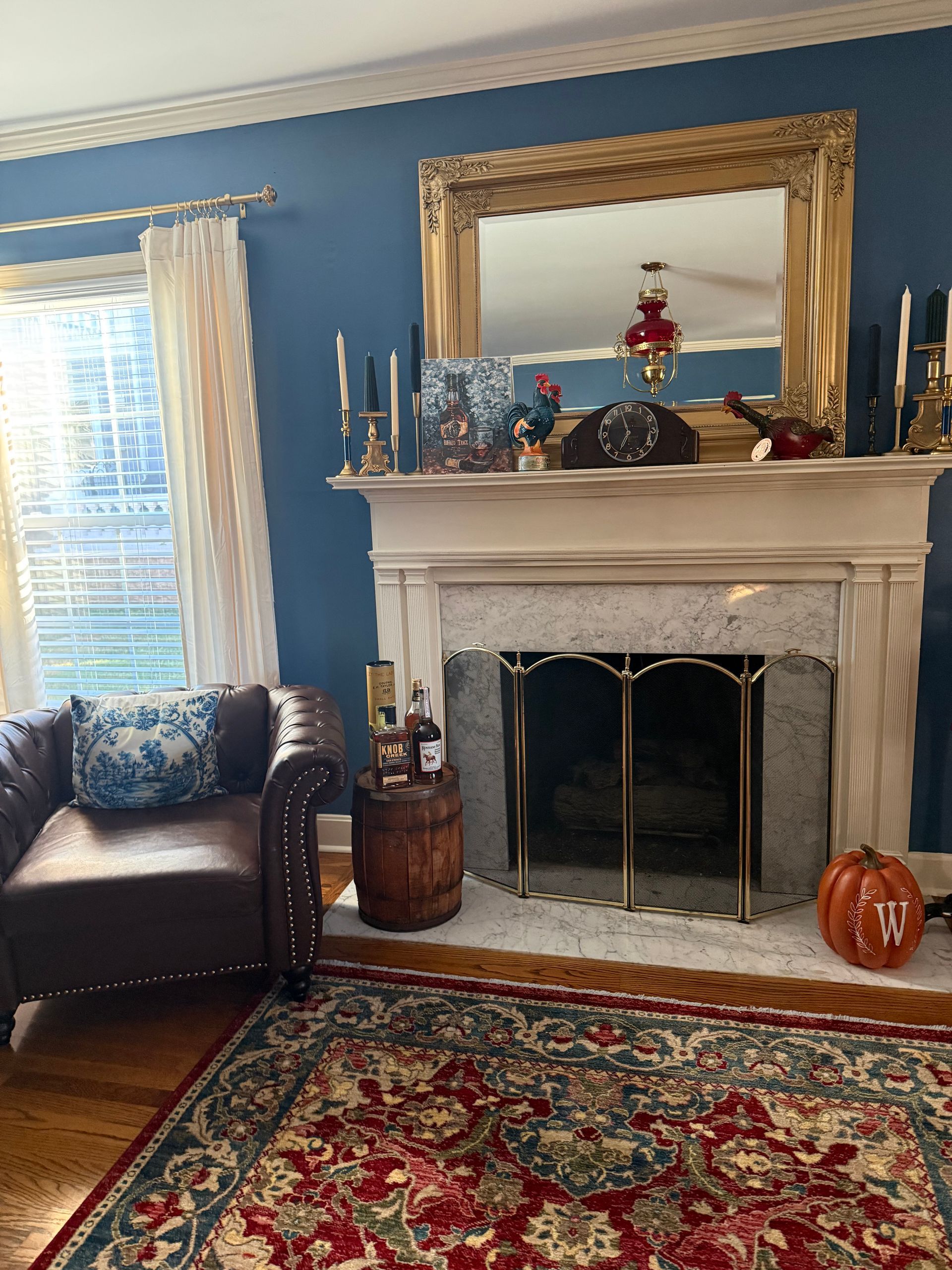 Cozy living room with blue walls, ornate fireplace, mirror, red patterned rug, and leather chair.