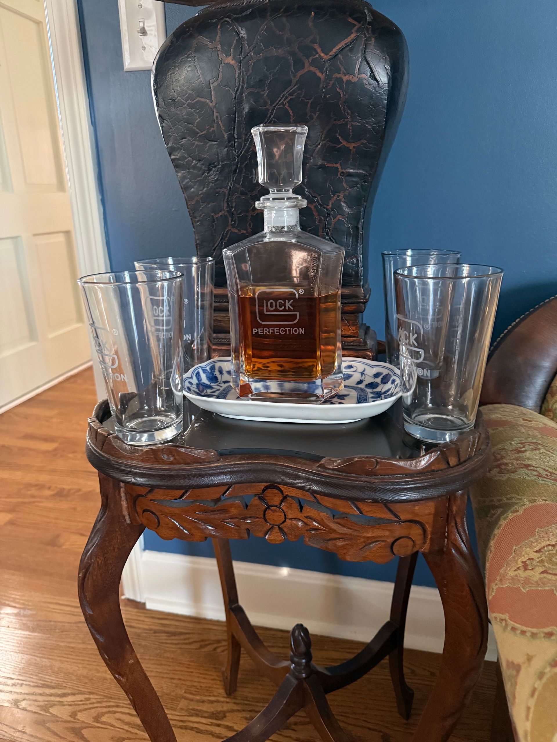 Whiskey decanter and two glasses on a small ornate side table in a living room chair.