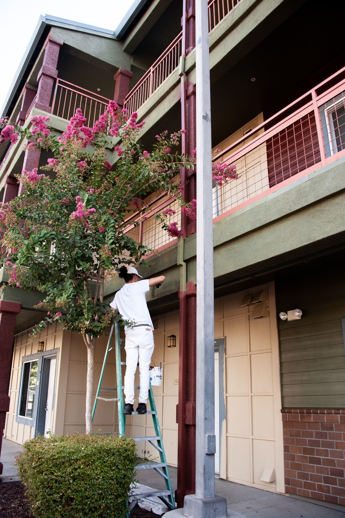 A man is standing on a ladder painting a building.