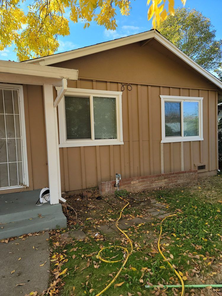 A brown house with white windows and a yellow hose in front of it.