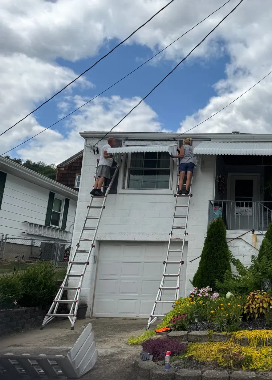 Two people on ladders working on the awning of a white building. Blue sky and power lines visible.