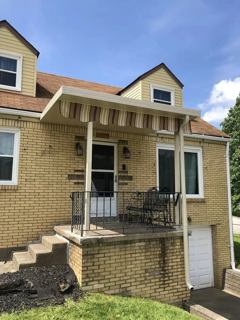 Yellow brick house with a front porch, awning, and steps.