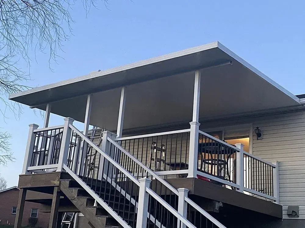 Deck with white railing and stairs, covered by a light-colored awning. A house is in the background.