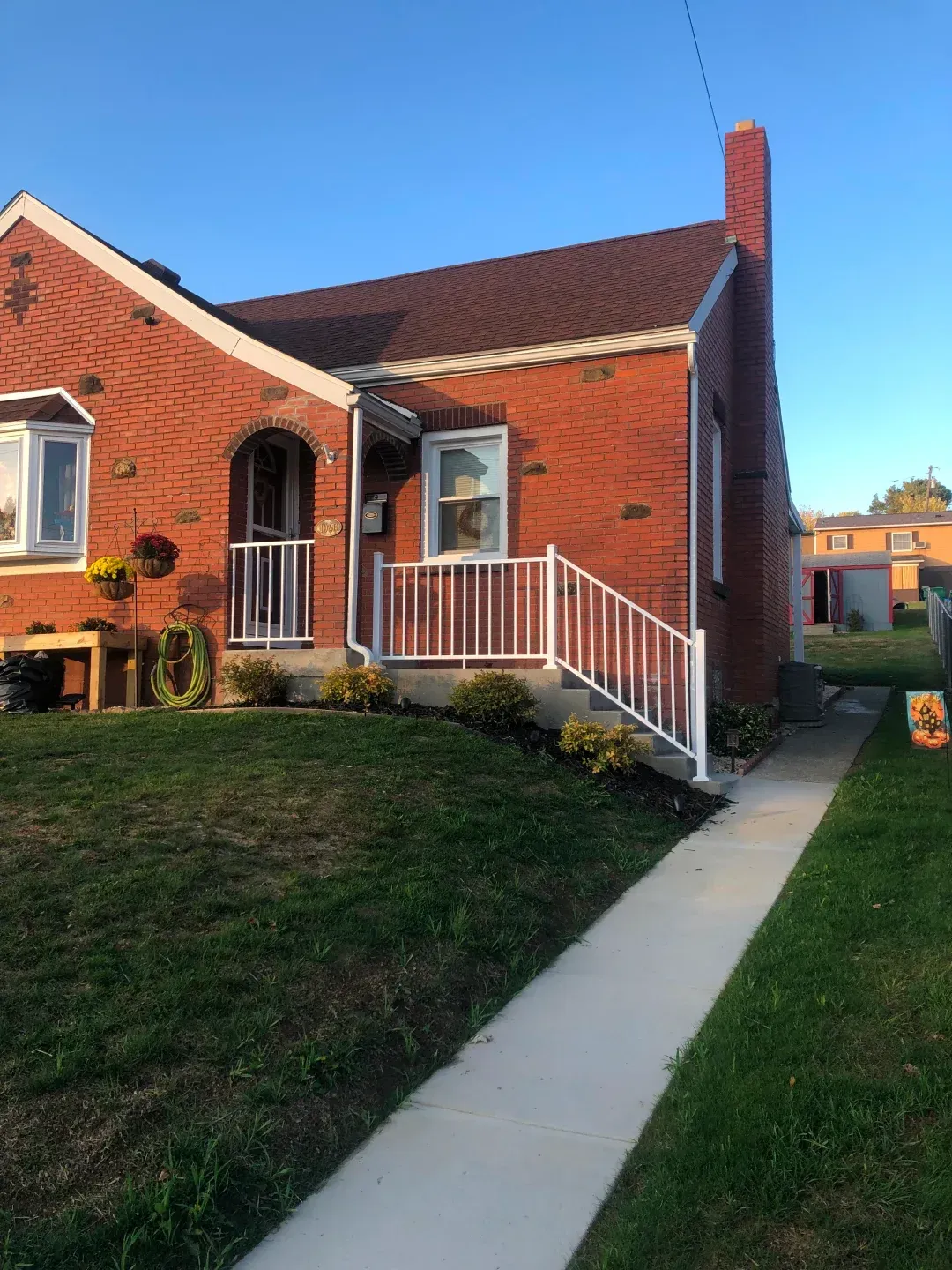 Red brick house with white railing and walkway. Green lawn.