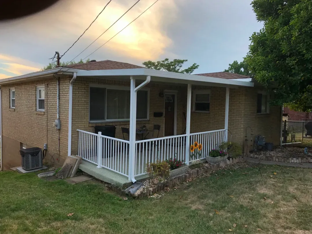A one-story brick house with a covered porch featuring white railing and a small yard.
