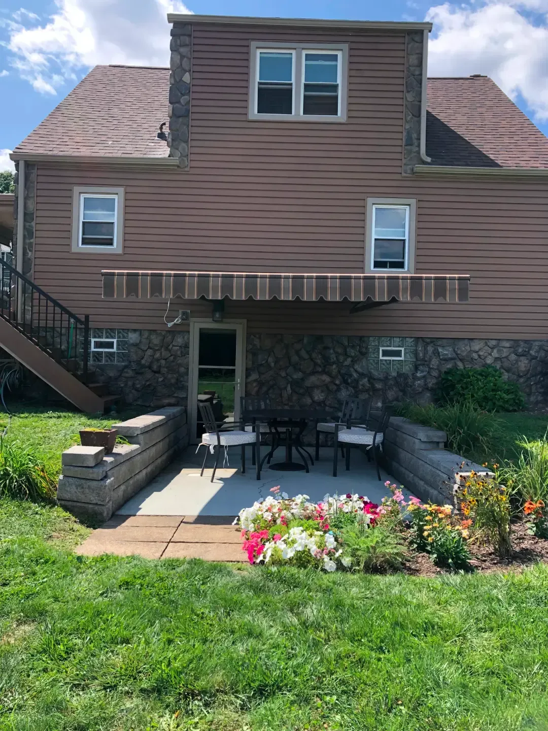 Backyard patio with flowers, a table and chairs, and a brown awning under the house.