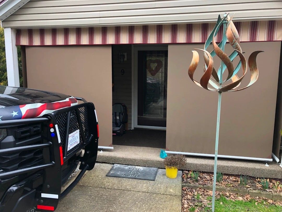 Beige sliding shade covers a doorway, a black vehicle is parked on the left, and a decorative metal sculpture on the right.