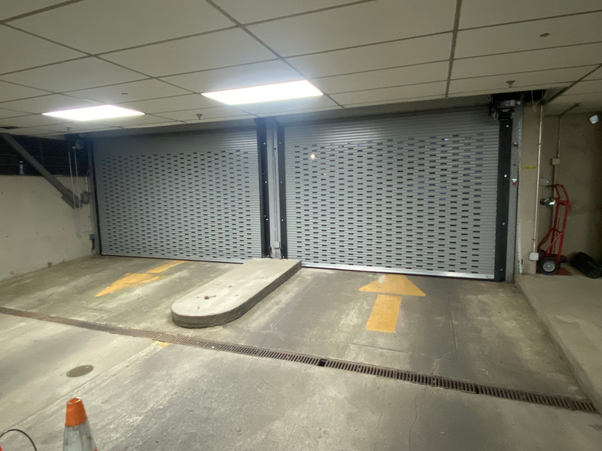 Rolling gray gate at a parking garage entrance, arrow pointing up, with overhead lighting.