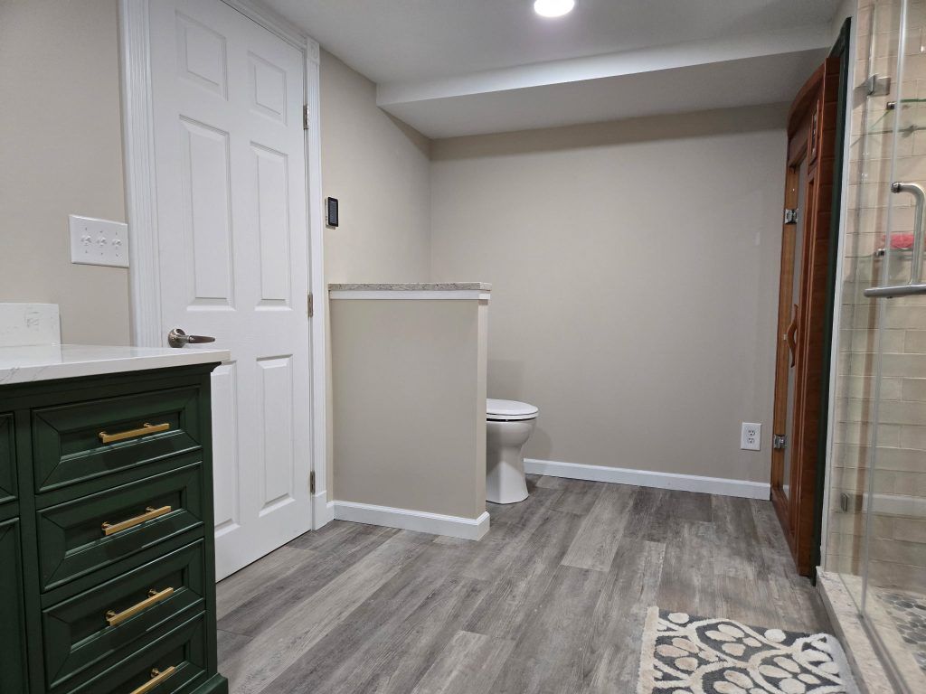 Empty hallway with gray wood flooring, beige walls, white door, green drawers, and a small rug.