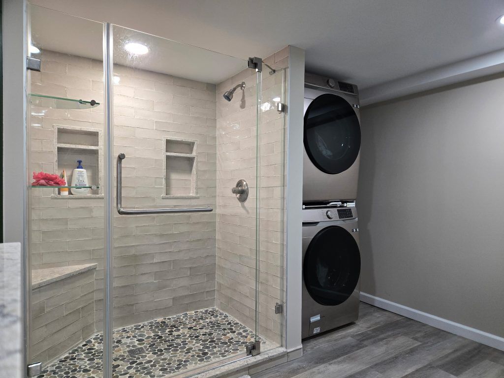 Modern bathroom with glass shower, pebble floor, and stacked washer-dryer beside it
