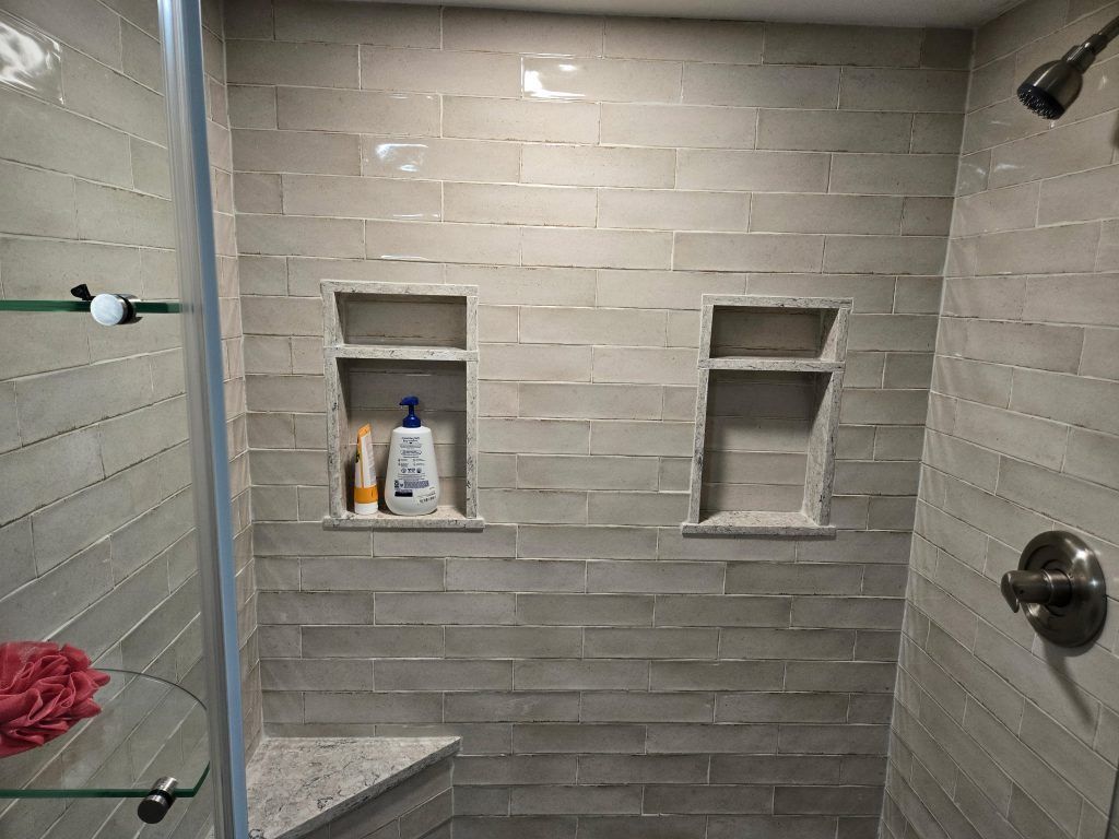 Tiled shower with built-in niches holding bottles, glass shelf, and wall-mounted shower fixtures