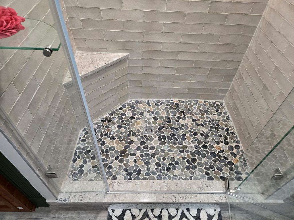 Small tiled shower stall with glass doors and pebble-pattern floor, viewed from above.