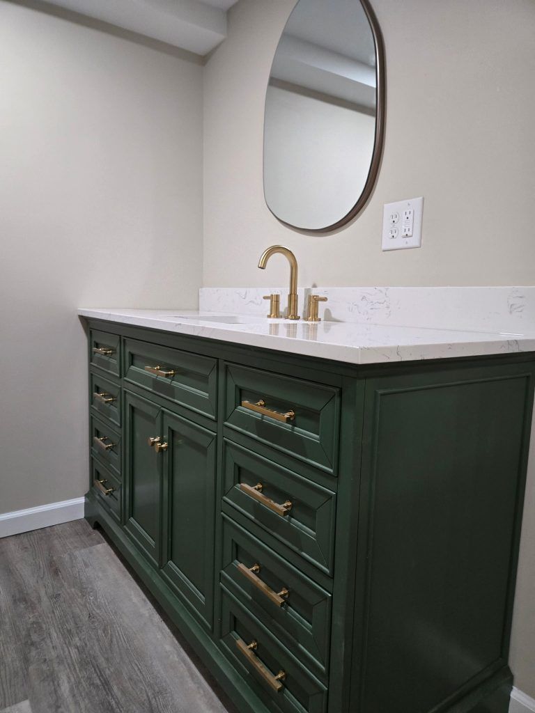 Dark green vanity with gold faucet and oval mirror in a light bathroom