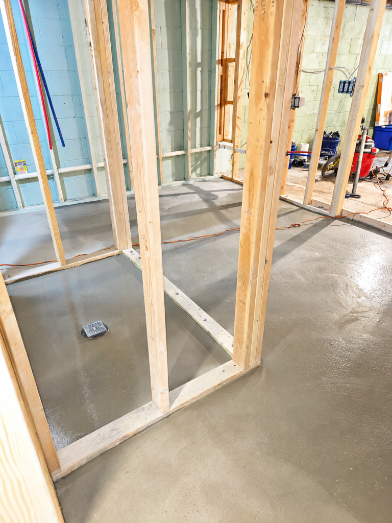 Wood-framed interior wall under construction with exposed studs and concrete floor
