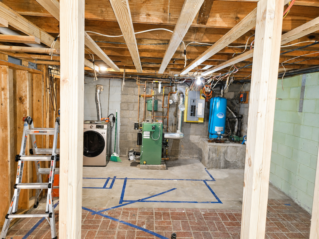 Unfinished basement with exposed joists, ladder, furnace, water heater, and tools on a concrete floor.