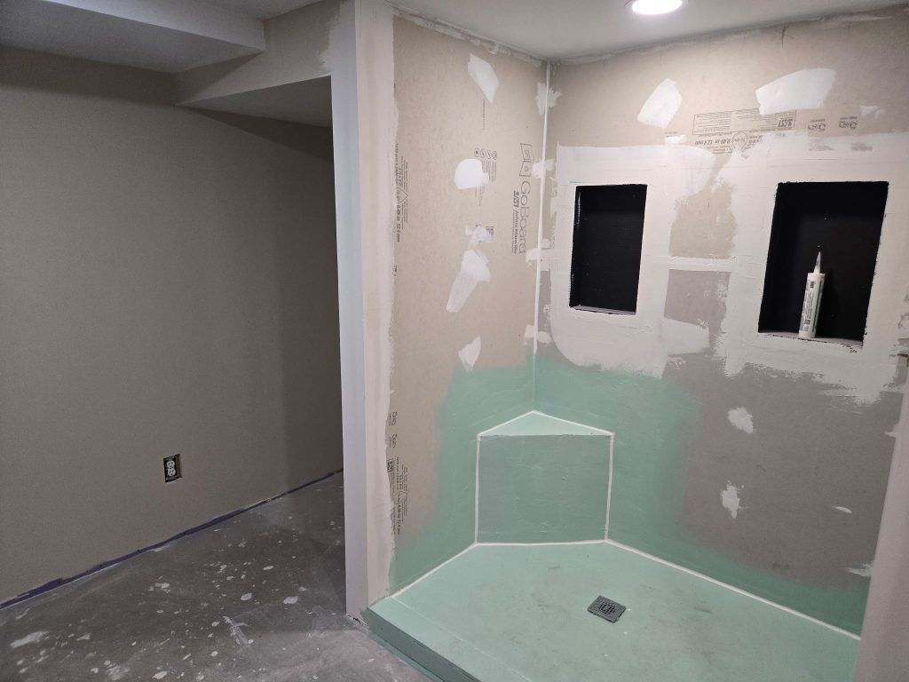 Partially renovated bathroom with tiled shower area and unfinished drywall walls