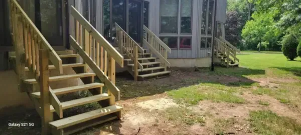 Wooden stairs leading to a building with glass doors, set beside a grassy yard and dirt path.