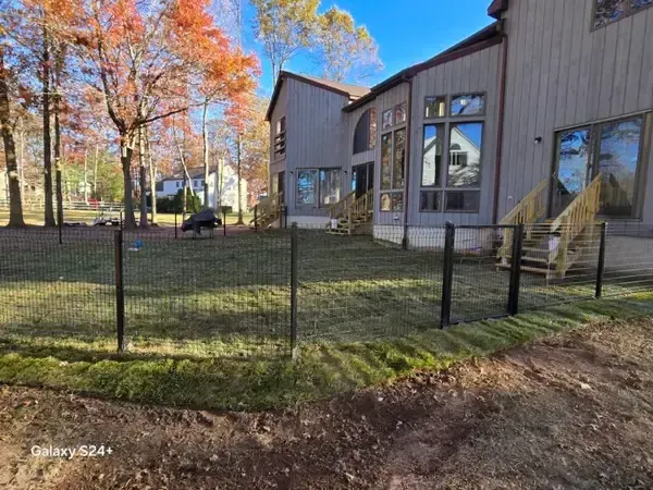 Modern house with large windows behind a black fence, set among autumn trees and grass