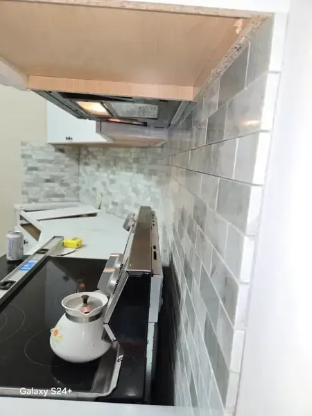 Kitchen stove with pot under a range hood, white tile backsplash, and countertop items nearby