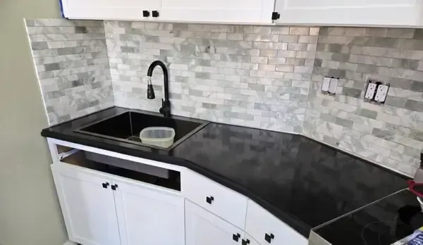 Modern kitchen corner with black countertop, white cabinets, sink, faucet, and gray tile backsplash