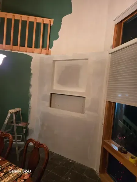 Partially painted wall with a recessed niche, window blinds, and dining chairs in a room