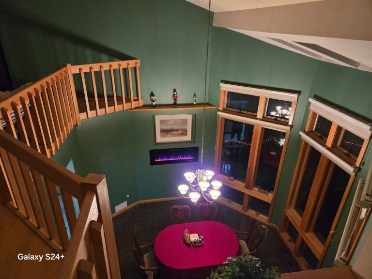 Loft living room with green walls, large windows, chandelier, and a red round table below a balcony railing