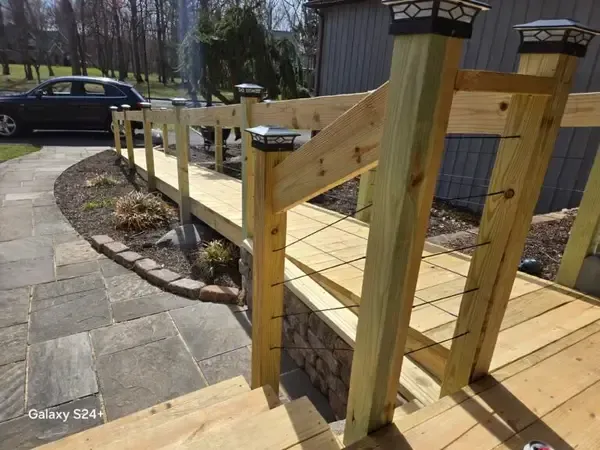 Wooden wheelchair ramp with railings beside a stone walkway and parked car outside a building