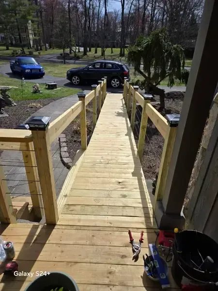 New wooden wheelchair ramp leading down to a driveway with parked cars and trees beyond
