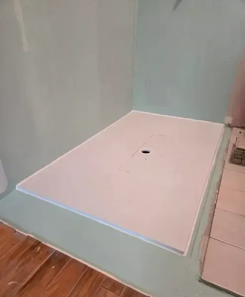 Empty pale-blue shower stall with a white shower base and drain hole in the center.