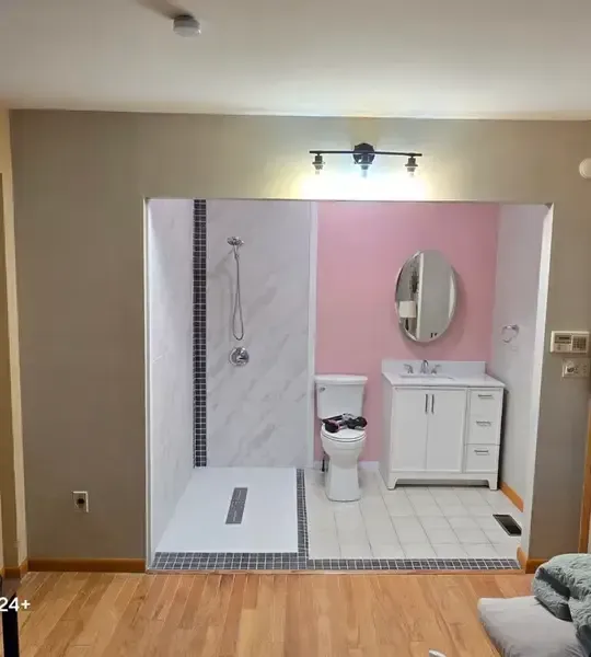 Bathroom remodel with white marble shower, pink accent wall, and vanity in a room with wood floors